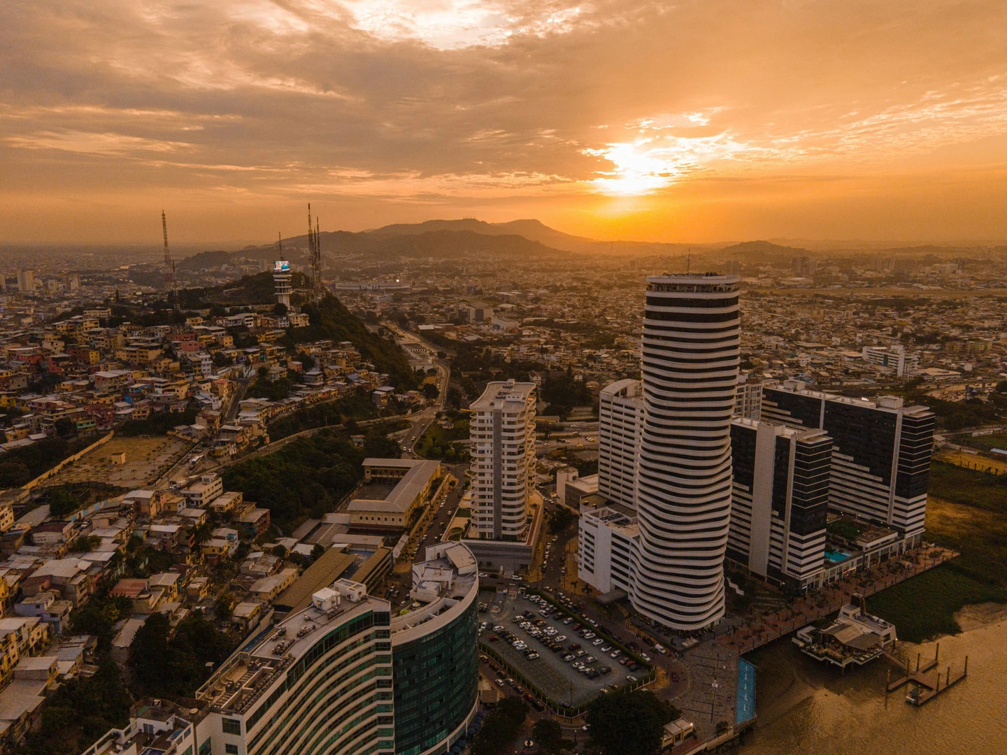 Vista aérea de una ciudad ecuatoriana al atardecer con rascacielos y colinas, simbolizando oportunidades de crecimiento. Mercurium Investech ofrece educación financiera y estrategias innovadoras para invertir en la bolsa de valores de Ecuador.